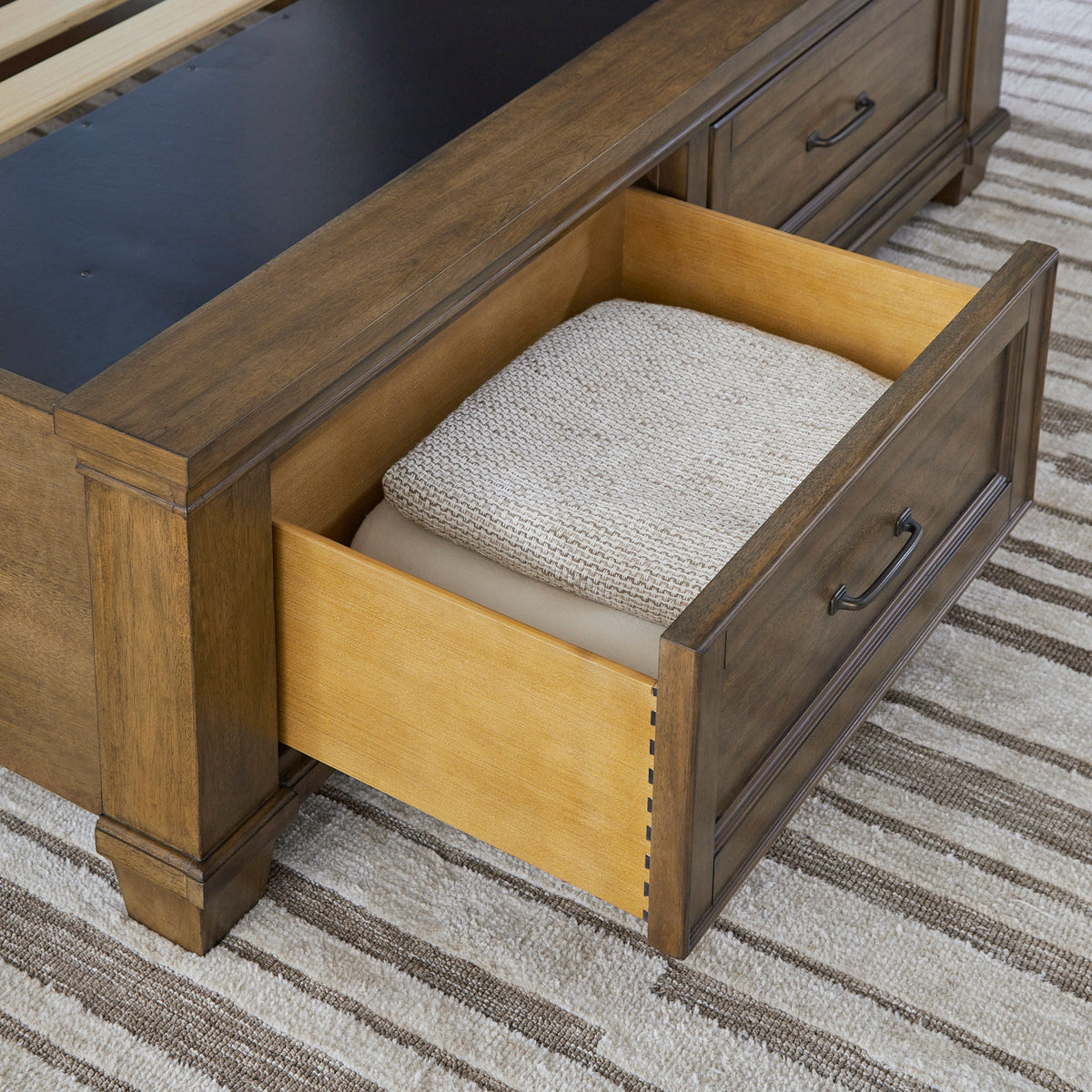 Open footboard storage drawer on the Pierson bed showing dovetail joinery and antique brass pull, holding folded blankets