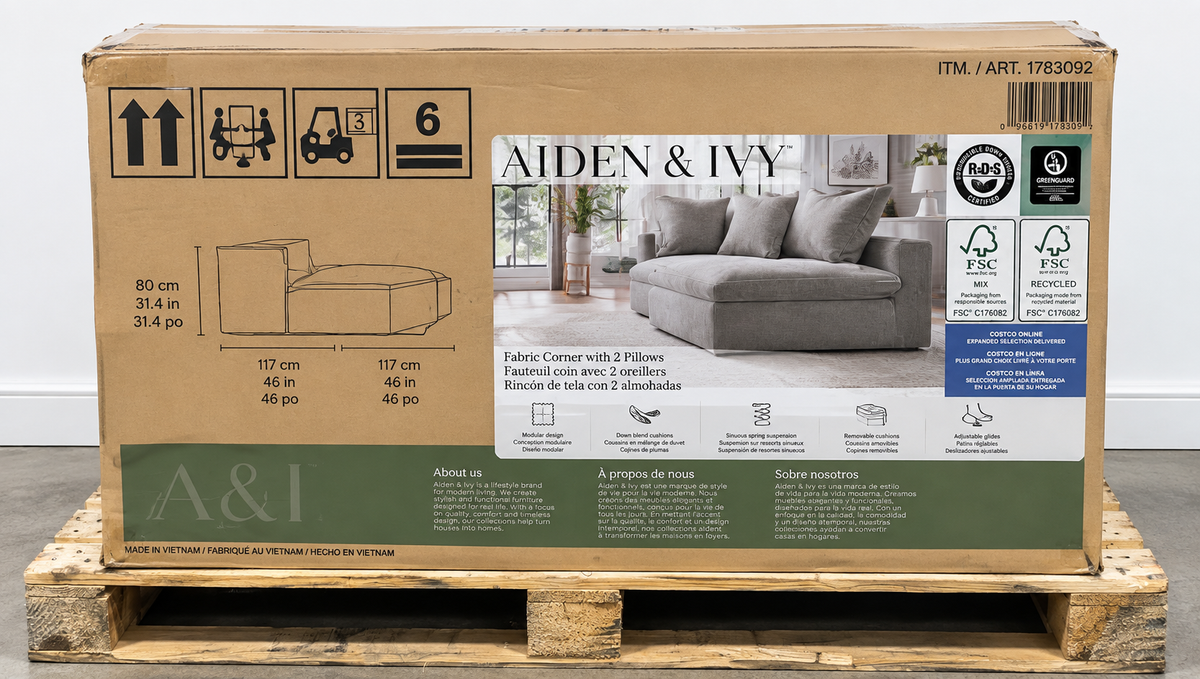 A large cardboard box for an Aiden & Ivy fabric corner sofa, displayed on a wooden pallet against a light gray background.