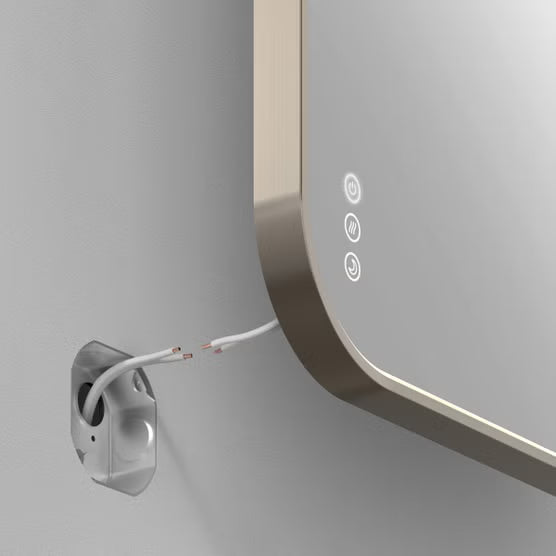 Close-up of a modern wall-mounted mirror with rounded edges, showing three circular touch control icons on the right side and a white power cable plugged into an outlet on the left against a light gray wall.
