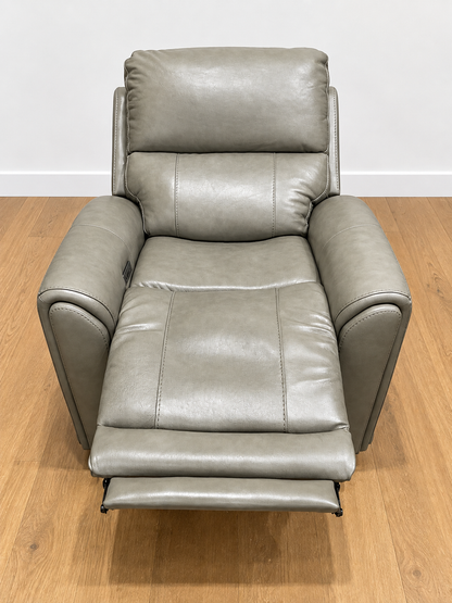A gray faux leather recliner chair with the footrest extended, set against a white wall and light brown wooden floor.