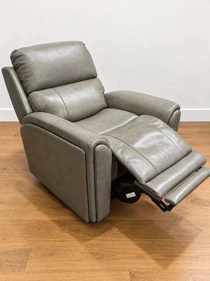 A gray faux leather recliner chair with the footrest extended, set on a light brown wooden floor against a plain white wall.
