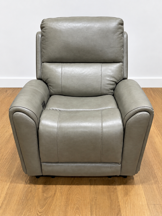 A gray upholstered recliner chair with padded backrest and armrests, photographed on a wood floor against a plain light wall.