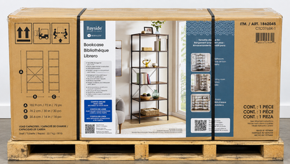 A Bayside Bookcase in its original cardboard packaging, displayed on a wooden pallet. The box features a large central label showing the black metal bookcase with books and decor, flanked by blue and white side panels with product details and shipping symbols.