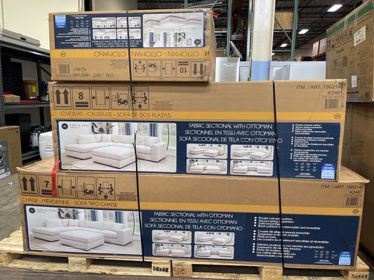 Stacked cardboard boxes of sectional sofa fabric options in a warehouse setting, with the front box showing a navy blue panel with product photos and text for fabric sections with ottomans.