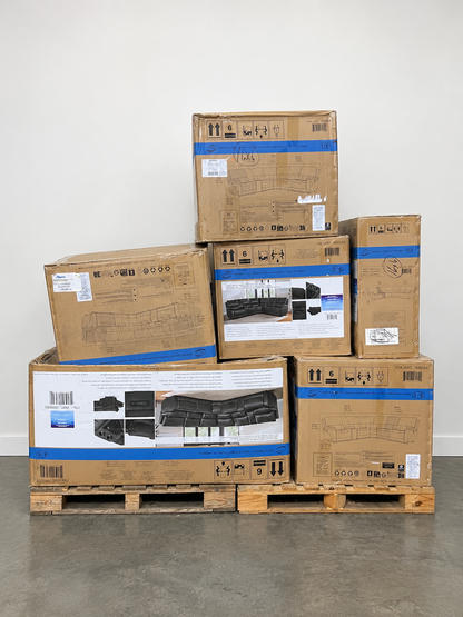 A stack of large cardboard boxes for furniture, secured with blue straps on wooden pallets in a warehouse setting with shelving visible in the background.