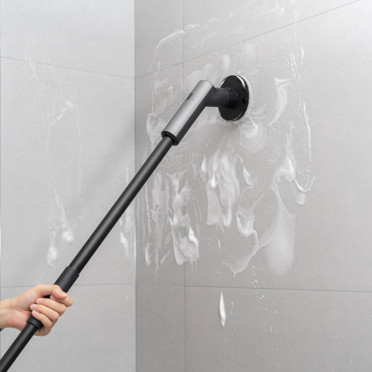 HOTO Cordless Spin Scrubber with the extension pole attached, scrubbing a soapy shower wall
