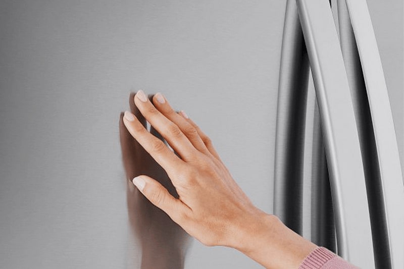 Close-up of a hand touching the smudge-resistant PrintProof stainless steel finish beside the door handle