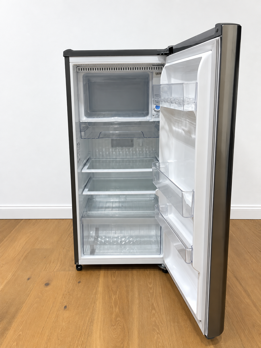 A compact top-freezer refrigerator with its door open, showing a white interior with multiple glass and plastic storage bins.