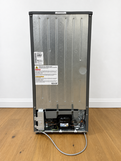 The back view of a tall stainless steel refrigerator or freezer, showing the vented metal back panel, warning labels, and exposed cooling components at the bottom.