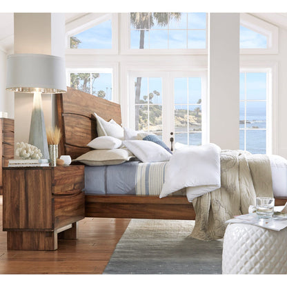 Modus Ocean nightstand beside a bed with lamp, showing the natural wood grain finish