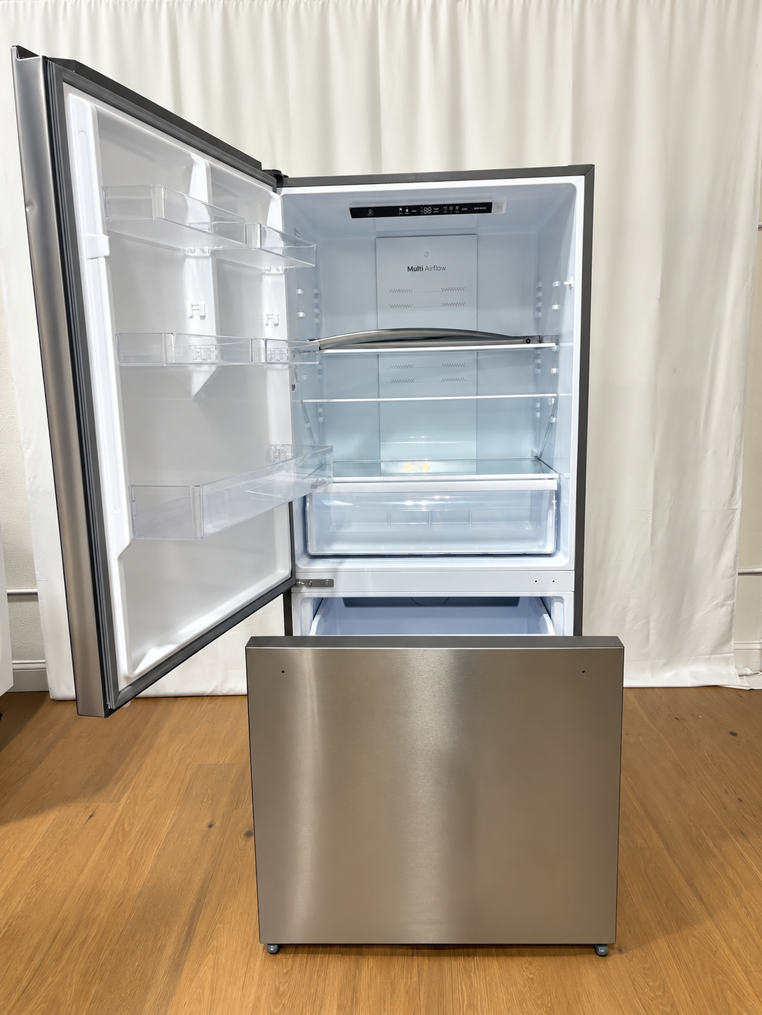 A stainless steel bottom-freezer refrigerator with its door open, showing the interior shelves and light box.