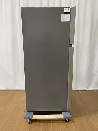 A tall, stainless steel top-freezer refrigerator on a wheeled dolly, photographed against a white curtain backdrop on a light wood floor.