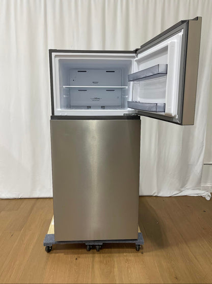A stainless steel top-freezer refrigerator on wheels, shown with the freezer door open to reveal the empty interior, set against a white curtain backdrop on a wooden floor.