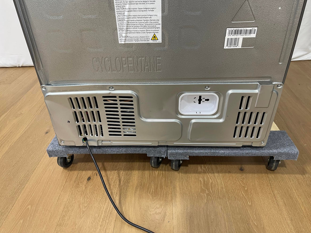 The back view of a stainless steel appliance, likely a refrigerator or freezer, resting on a gray wheeled dolly over a light wood floor.
