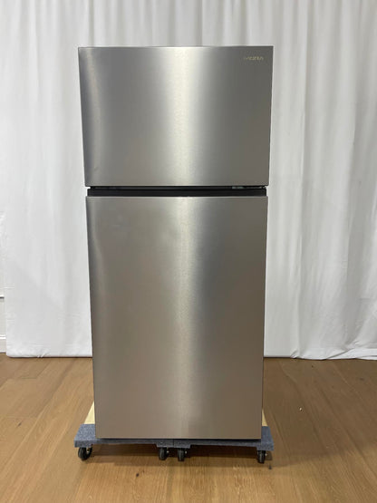 A stainless steel top-freezer refrigerator on a dolly with casters, standing on a wooden floor against a white curtain backdrop.