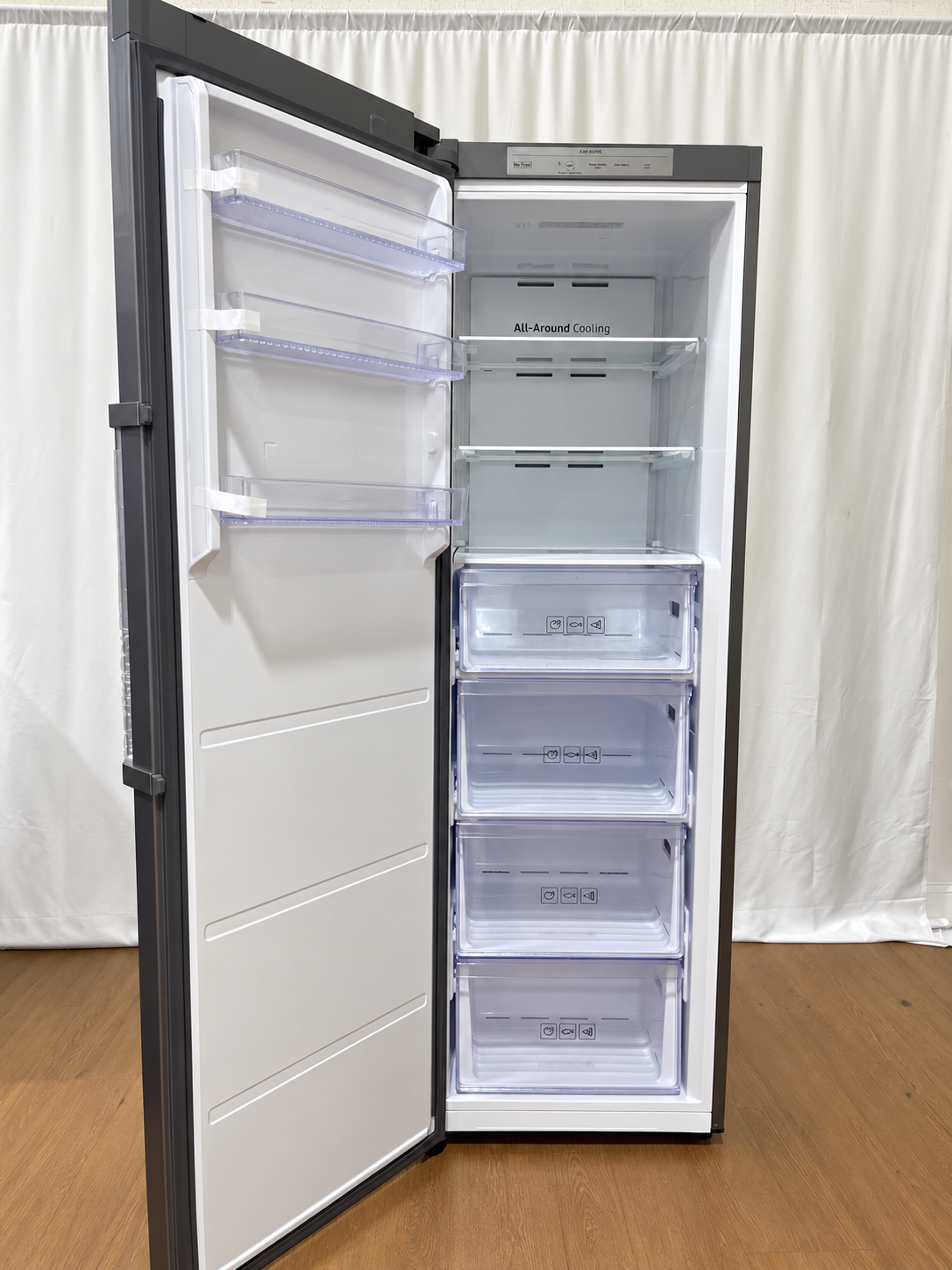 A tall, narrow refrigerator with its door open, showing a white interior with multiple transparent storage drawers and shelves.